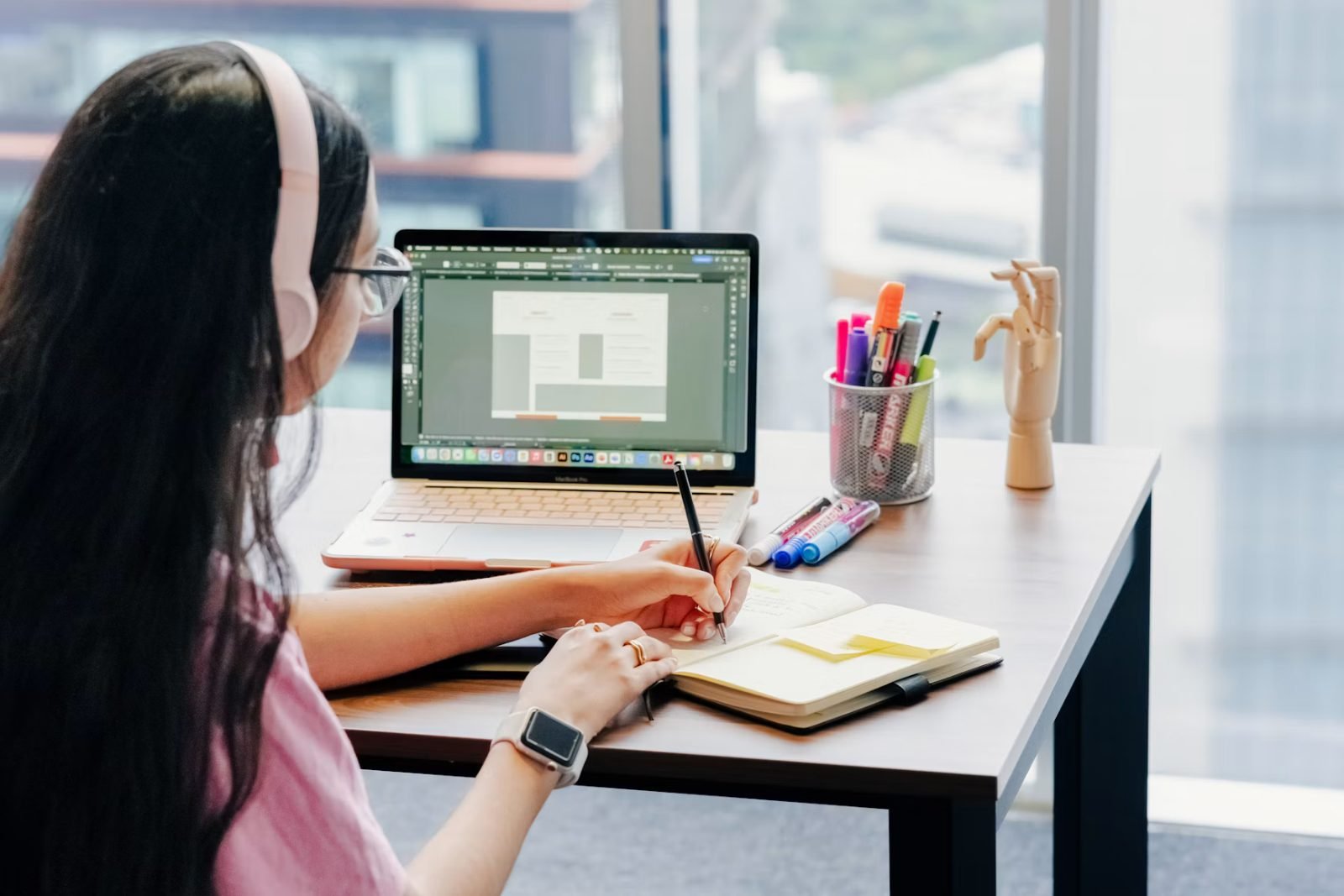 Designer gráfico trabalhando no notebook com um software de design aberto enquanto anota ideias num caderno